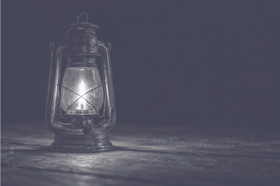 A lit oil lantern glowing on a wooden floor in the dark