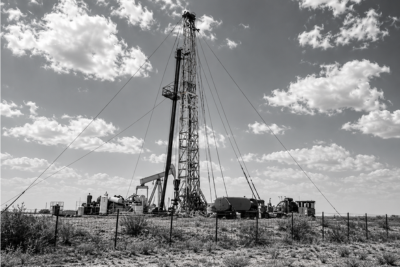 A drilling rig and pumpjack on flat scrubland under a wide sky