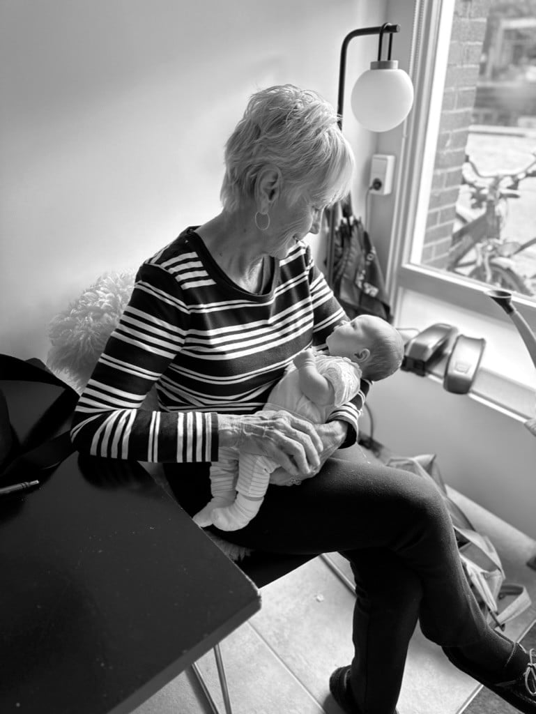 A grandmother holding her newborn granddaughter by a window