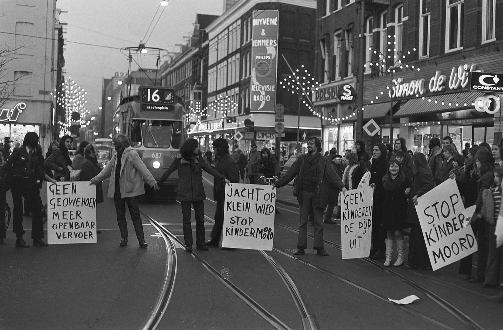 Demonstrators holding hands across tram tracks in front of tram 16 with Stop Kindermoord placards, Amsterdam 1972