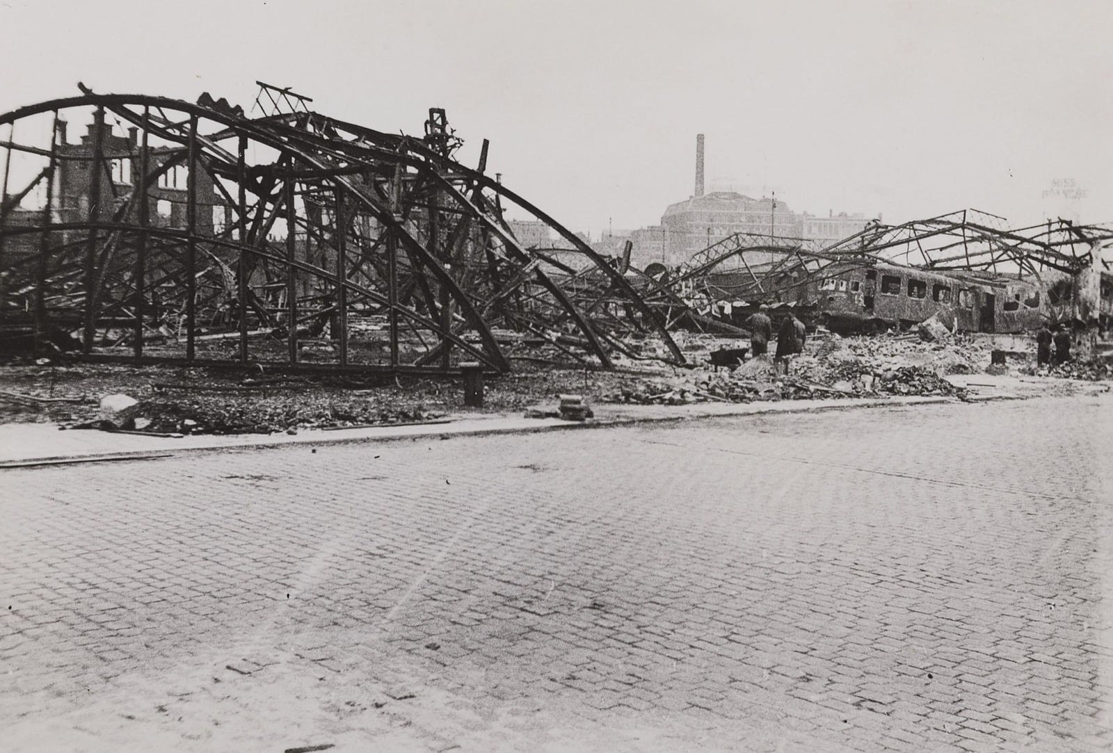Ruins of Rotterdam's Maas station in 1940 with a wrecked train and a brick street in the foreground